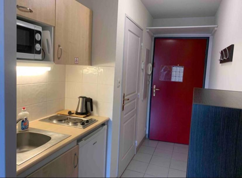- une cuisine avec une porte rouge et un évier dans l'établissement Studio - face de l’hôpital nord, à Saint-Priest-en-Jarez