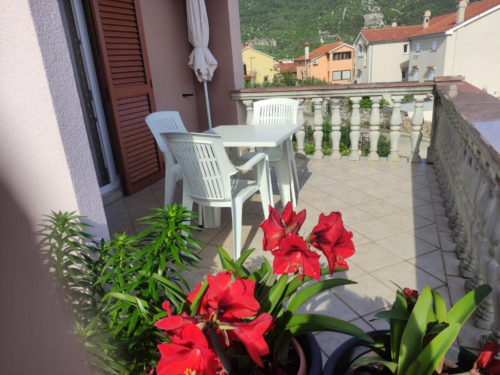 2 Stühle und ein Tisch auf einem Balkon mit roten Blumen in der Unterkunft Apartman Budimir1 in Cres