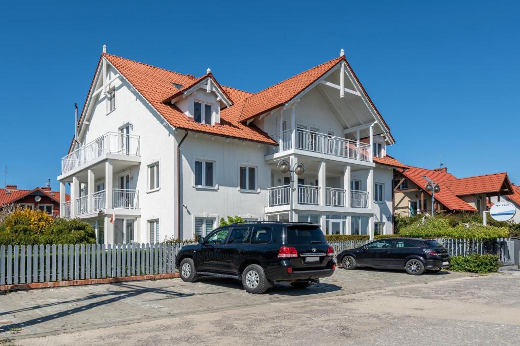 une grande maison blanche avec des voitures garées devant elle dans l'établissement PIONOW Rodzinne Apartamenty Urocza 10, à Krynica Morska