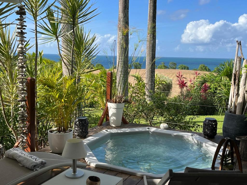a hot tub in a garden with palm trees and the ocean at Indigo Palmes in Sainte-Rose