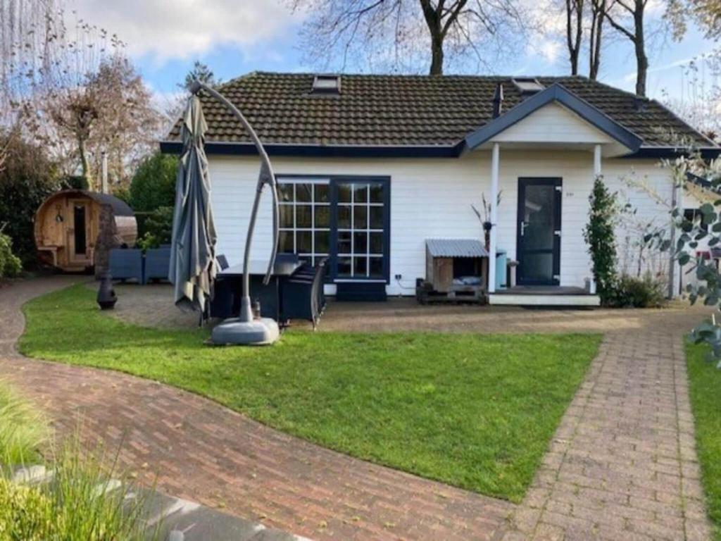 a white house with a playground in the yard at Cosy forest cabin with a barrel sauna in Voorthuizen