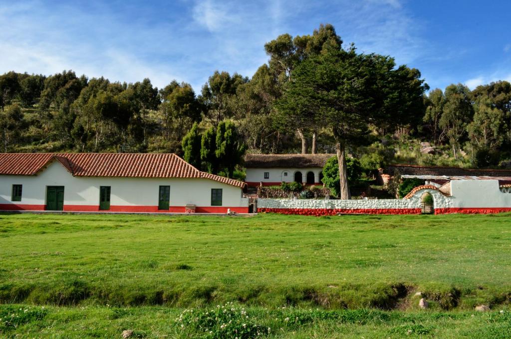 una casa blanca con un campo verde y árboles en Fundo Chincheros Lodge en Juliaca