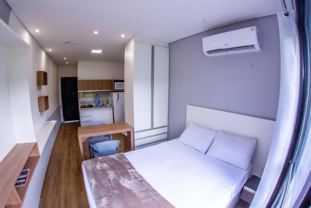 a small bedroom with a white bed and a kitchen at Flat - Mini House in Lagoa Santa