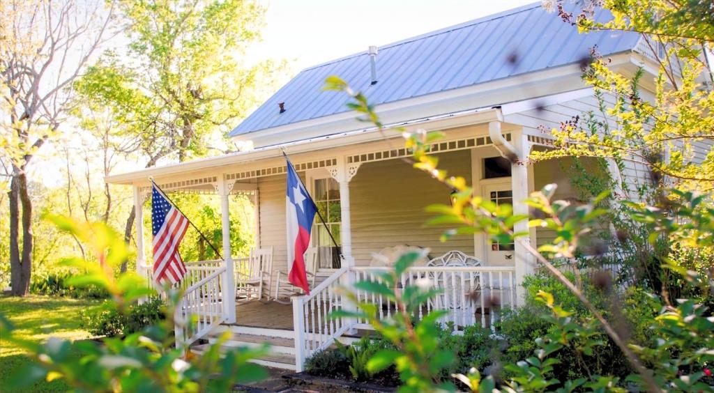 a house with two flags on the front porch at Circa 1900 - Historic - Romantic - Private - Pond - Fenced Yard - The Cottage at Chappell Hill in Chappell Hill