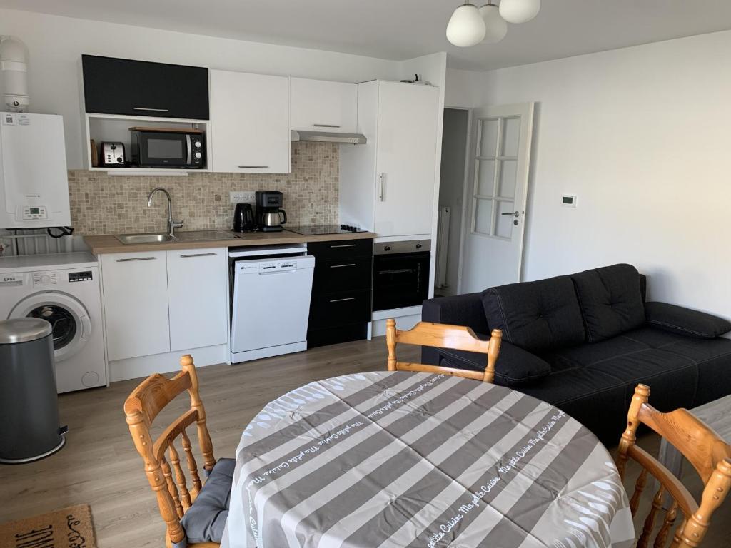 un salon avec un canapé noir et une cuisine dans l'établissement Appartement Neuf Centre-Ville Fort-Mahon-Plage avec Balcon et Parking, Idéal Famille - FR-1-482-114, à Fort-Mahon-Plage