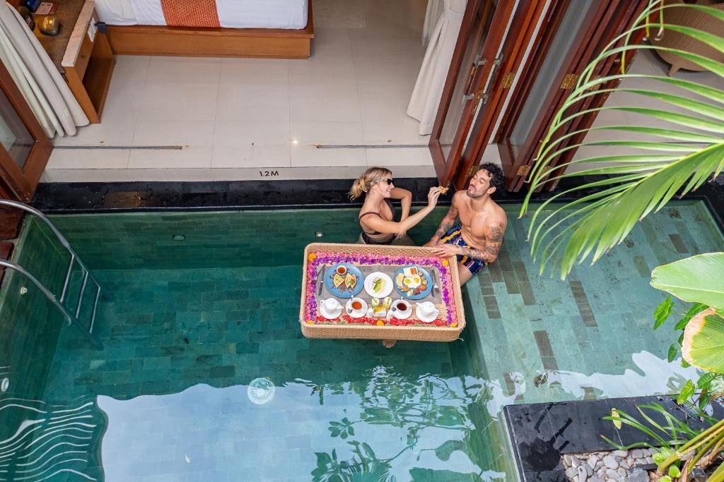 two people sitting in a pool with a suitcase in the water at Seminyak Sanctuary Villa by Ini Vie Hospitality in Legian