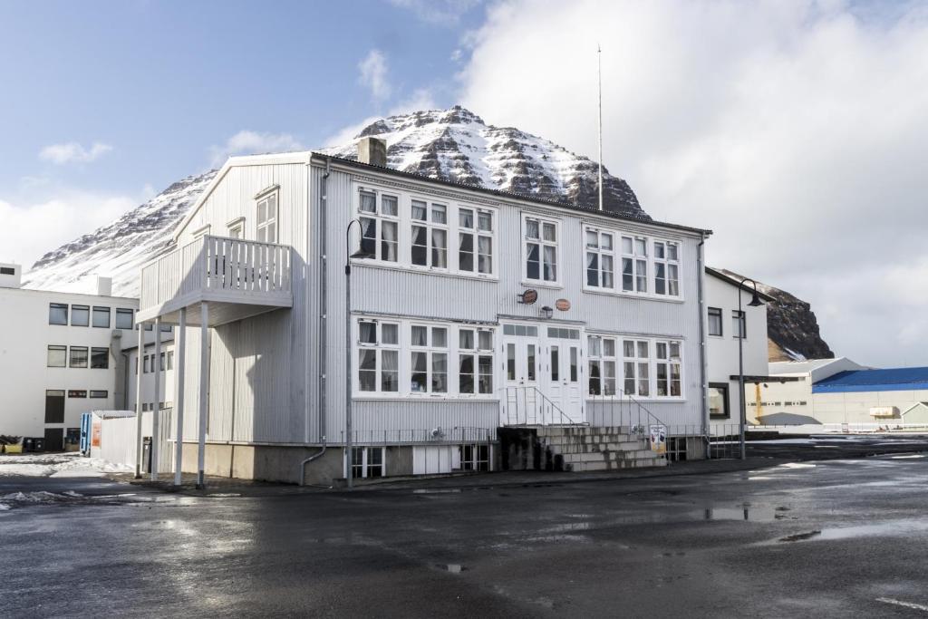 un edificio bianco con una montagna coperta di neve dietro di esso di Einarshúsid Guesthouse a Bolungarvík