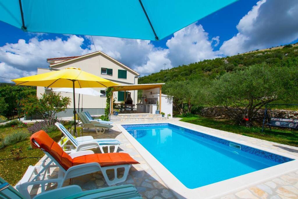 a pool with chairs and an umbrella next to a house at House Duje in Plano