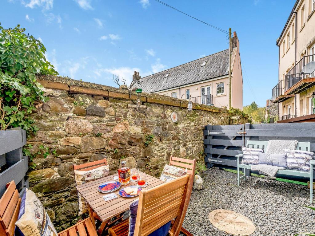 a patio with a table and chairs and a stone wall at Harbour Retreat in Garlieston