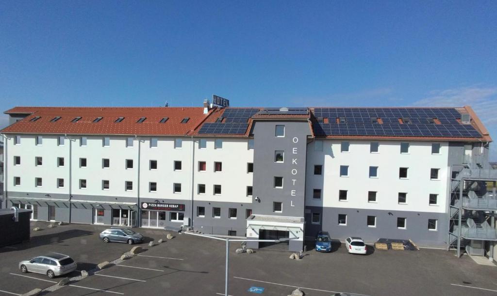 un gran edificio blanco con coches aparcados en un aparcamiento en OEKOTEL Treffpunkt Föhrenhain en Föhrenhain