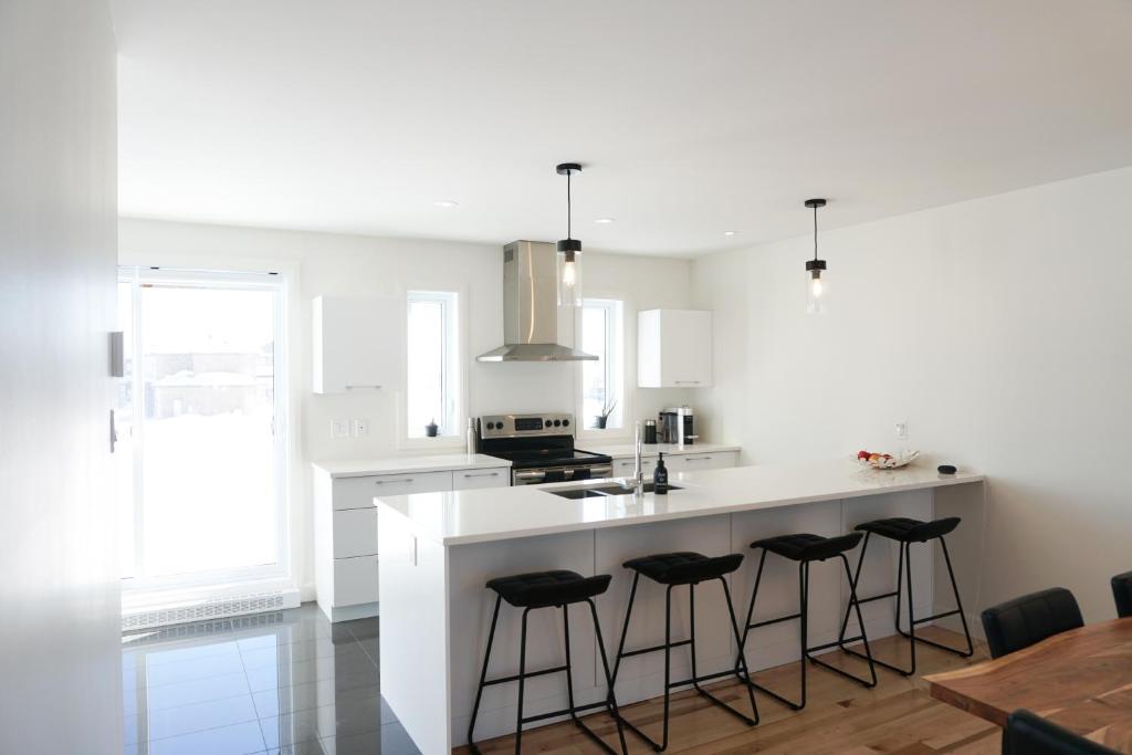 kuchnia z białym blatem i barowymi stołkami w obiekcie Le Citadin - Maison neuve moderne & ensoleillée w mieście Quebec City