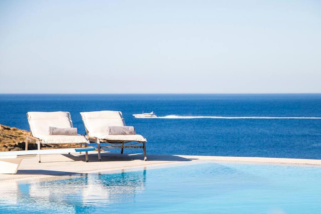 two chairs sitting next to a swimming pool with the ocean at Villa Anatoli in Mýkonos City