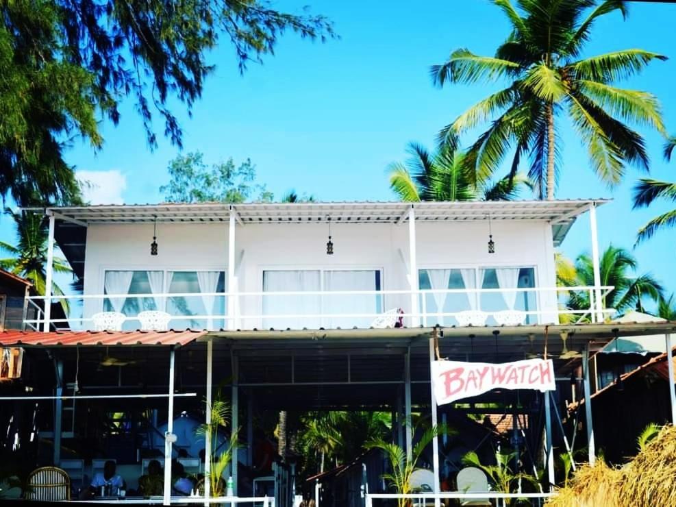 a white building with palm trees in front of it at Baywatch Beach Resort patnem in Canacona