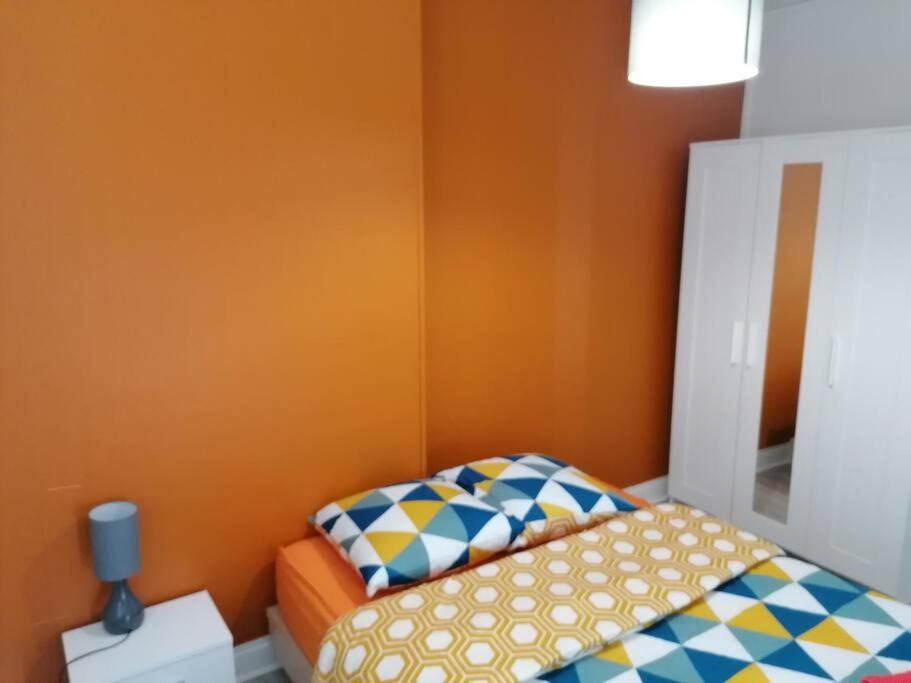 a small bedroom with a bed and an orange wall at Appartement meublé proche du centre - Wifi&#47;Parking in Clermont-Ferrand