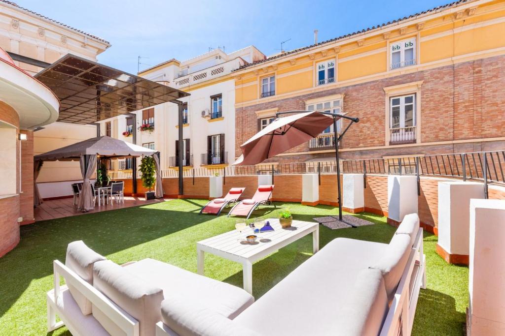 a patio with white couches and a table and umbrella at GRAN TERRAZA CON VISTAS A CALLE LARIOS in Málaga