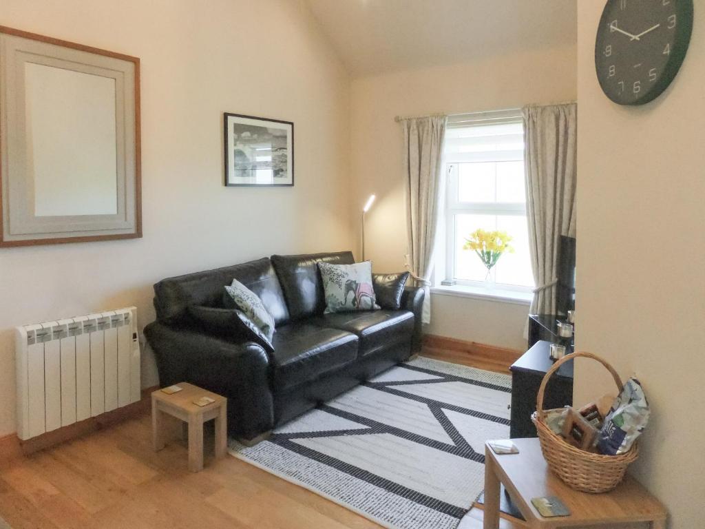 a living room with a black leather couch and a window at Kilbride Cottage in Pollachar