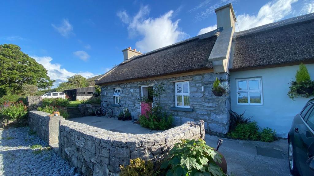a stone house with a stone retaining wall at Oranuisce Thatch Cottage Ballyvaughan in Ballyvaughan