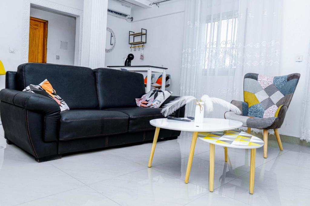 ein Wohnzimmer mit einem schwarzen Sofa und 2 Stühlen in der Unterkunft NAIVELI-PALM Appartement meublé sobre et chic in Douala