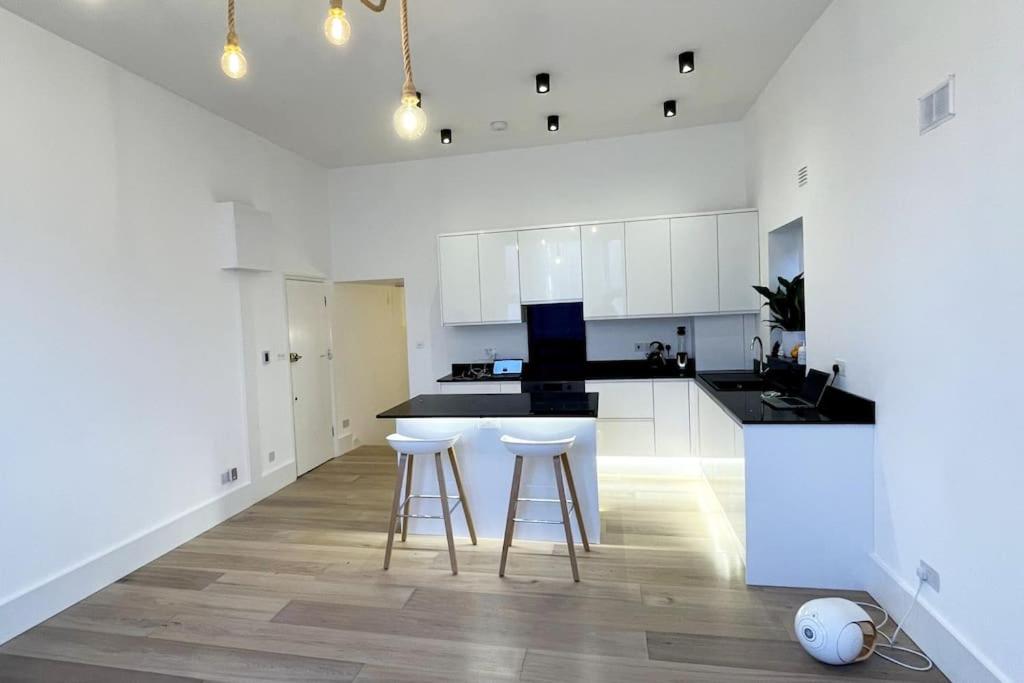 a kitchen with white cabinets and bar stools at Beautiful brand-new flat in London