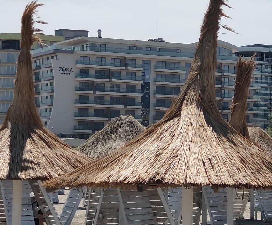 a group of straw umbrellas in front of a building at L&C BEACH HOME by ZORA Rezidential - PE PLAJA in Mamaia Sat/Năvodari