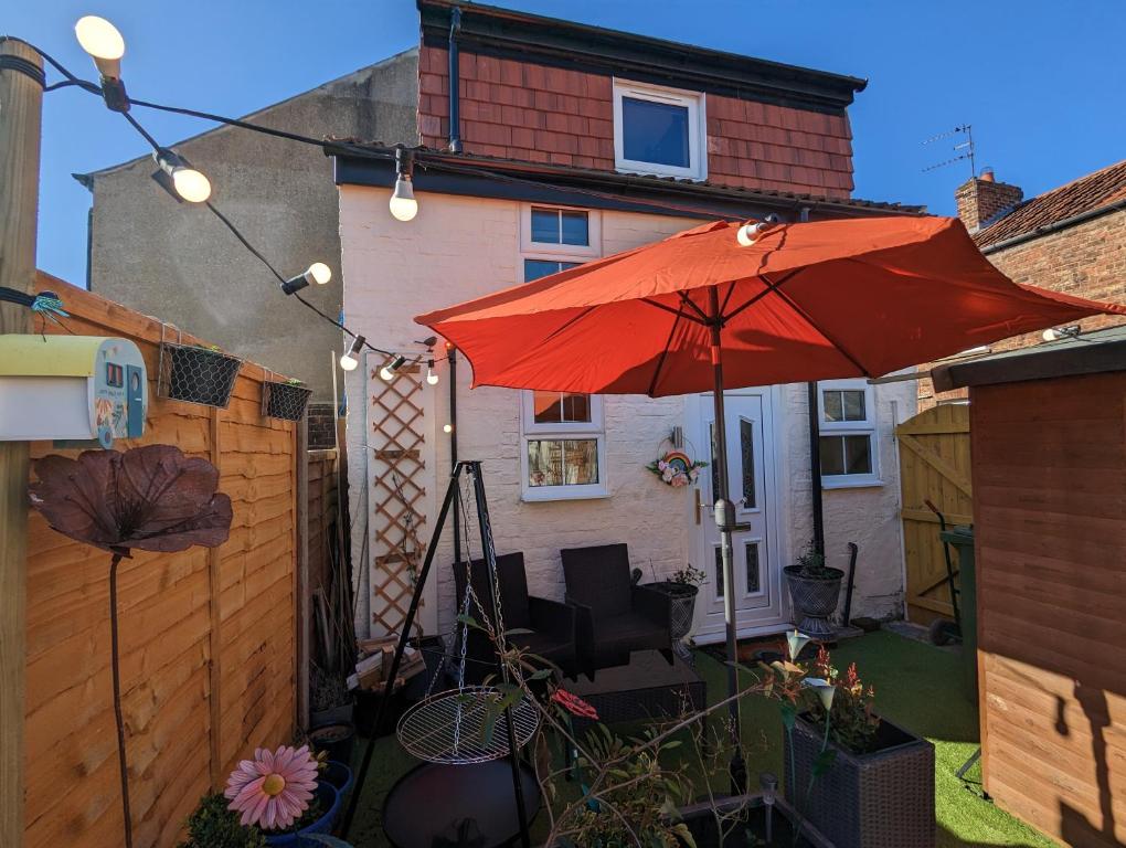 a patio with a red umbrella and chairs and a fence at Flemingate Cottage, Beverley in Beverley