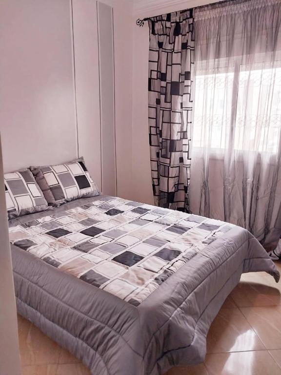 a bedroom with a bed with a checkered blanket and a window at Appartement Martil , très proche de la plage in Martil