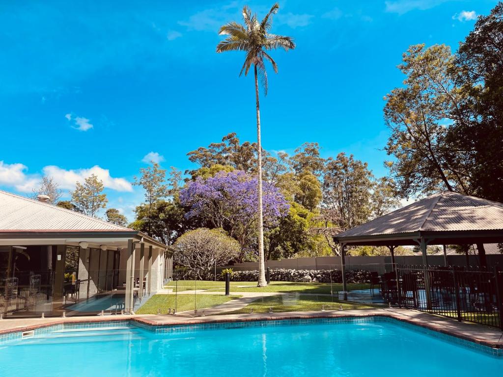 una palmera frente a una casa con piscina en Invercauld House en Goonellabah