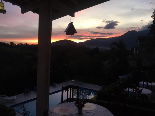uma vista para o pôr-do-sol a partir de um alpendre com vista para as montanhas em Recanto dos Passáros Penedo RJ em Penedo