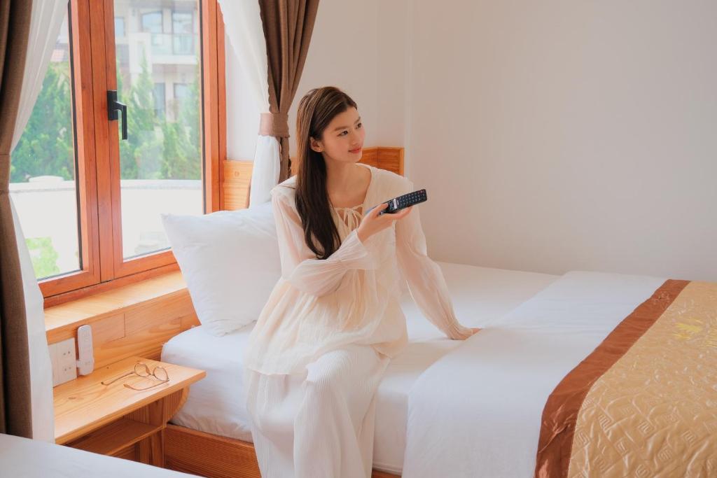 a woman sitting on a bed holding a remote control at Hoàng Yến Villa Dalat in Da Lat