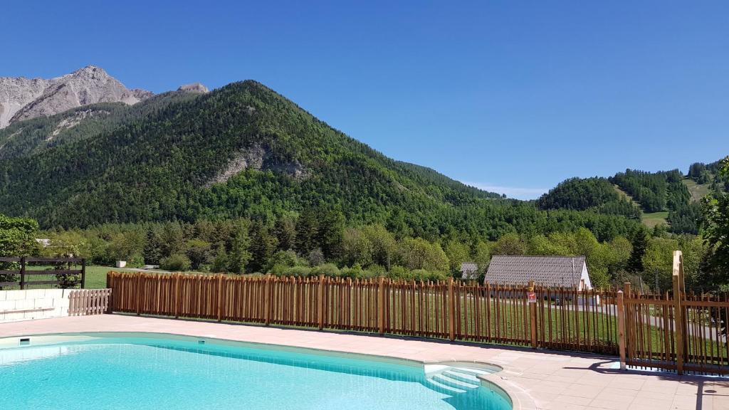 a swimming pool with a fence and mountains in the background at Camping les Auches in Ancelle