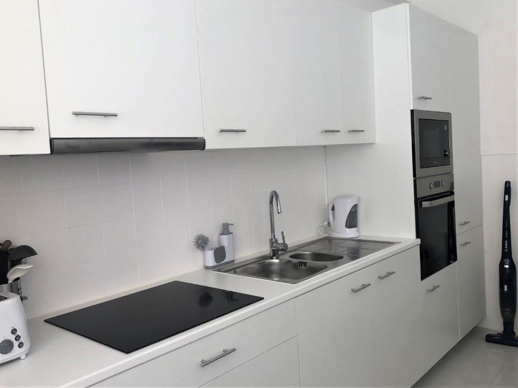 Una cocina blanca con fregadero y microondas. en Charming Apartment- Peniche, en Consolacao