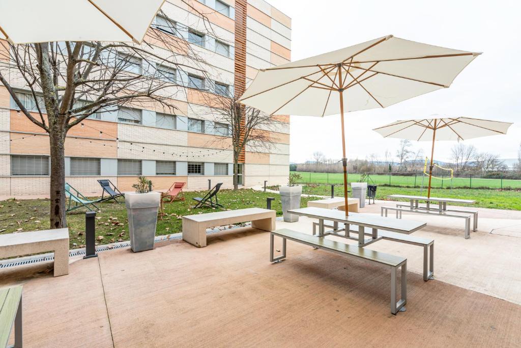 eine Gruppe von Bänken mit Sonnenschirmen vor einem Gebäude in der Unterkunft Residencia Universitaria Los Abedules in Pamplona