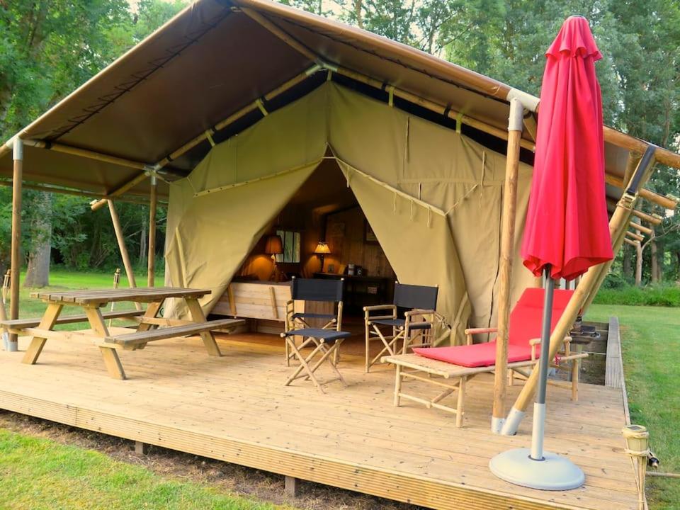 a tent with tables and chairs and a red umbrella at Tentes Safari aux Gîtes de Cormenin in Saint-Hilaire-sur-Puiseaux