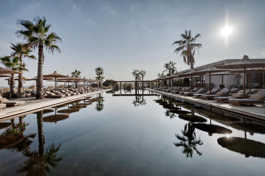 a pool at a resort with chairs and palm trees at Domes Zeen Chania, a Luxury Collection Resort, Crete in Kato Daratso