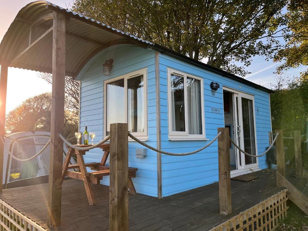 a blue tiny house with a table on a deck at Coral Shepherds Hut in Penally