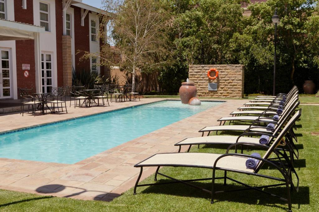 a row of lounge chairs next to a swimming pool at Protea Hotel by Marriott Bloemfontein in Bloemfontein