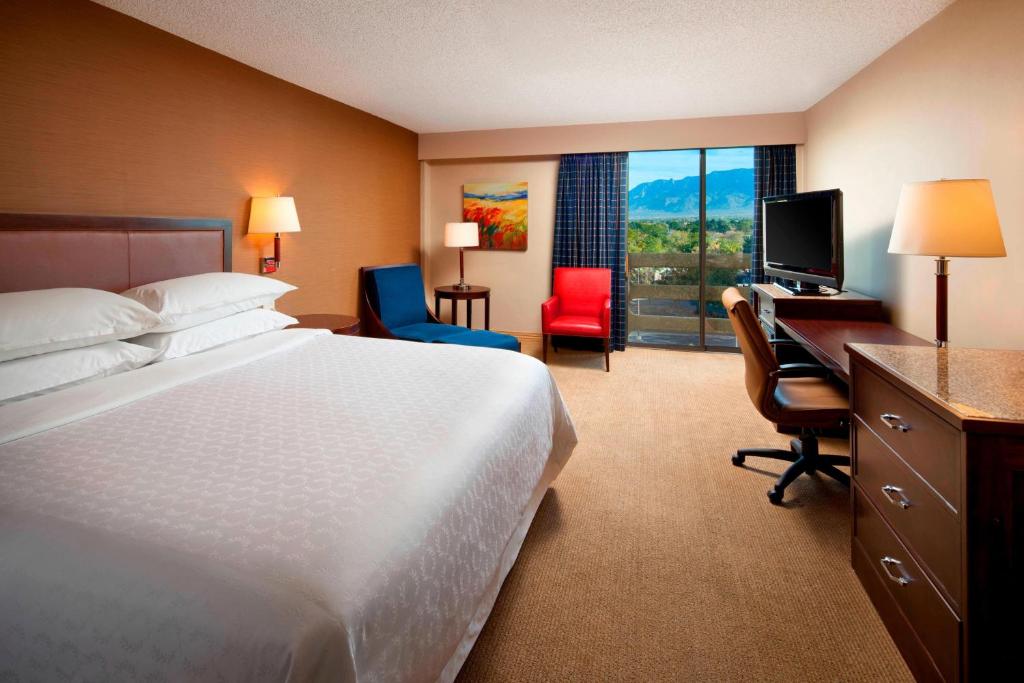 a hotel room with a bed and a desk with a computer at Sheraton Albuquerque Uptown by Marriott in Albuquerque