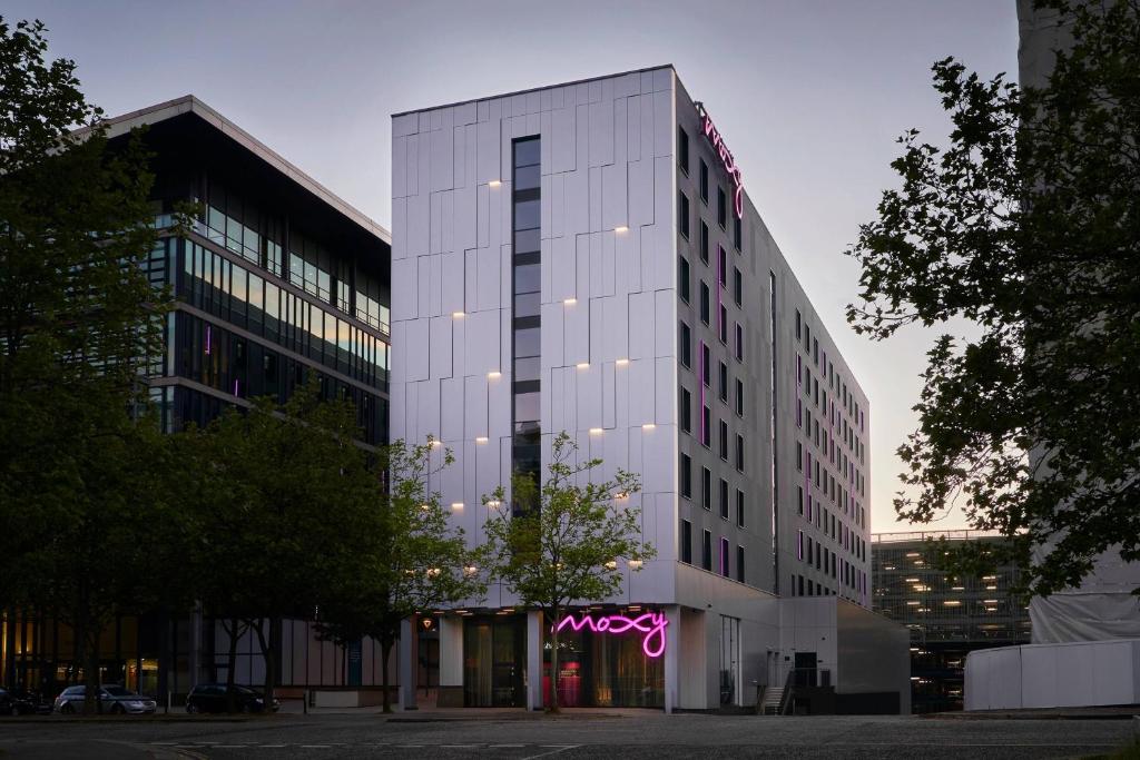 a tall white building with a neon sign on it at Moxy Milton Keynes in Milton Keynes