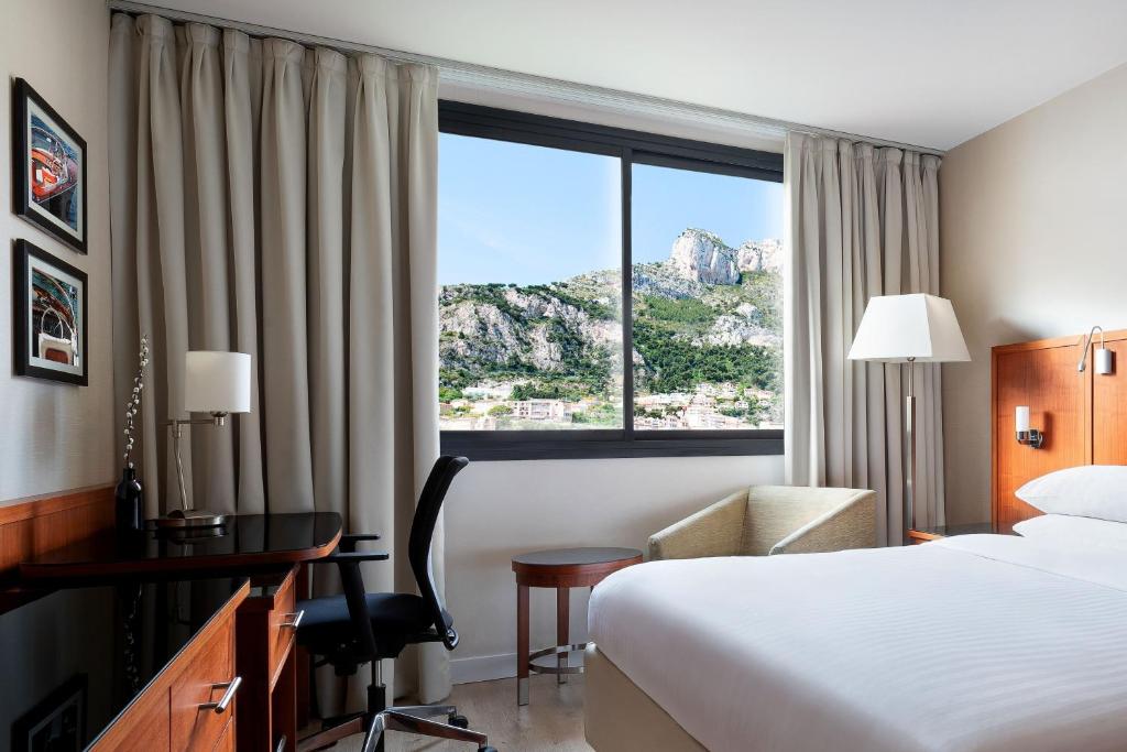 a hotel room with a bed and a desk and a window at Riviera Marriott Hotel La Porte De Monaco in Cap d'Ail