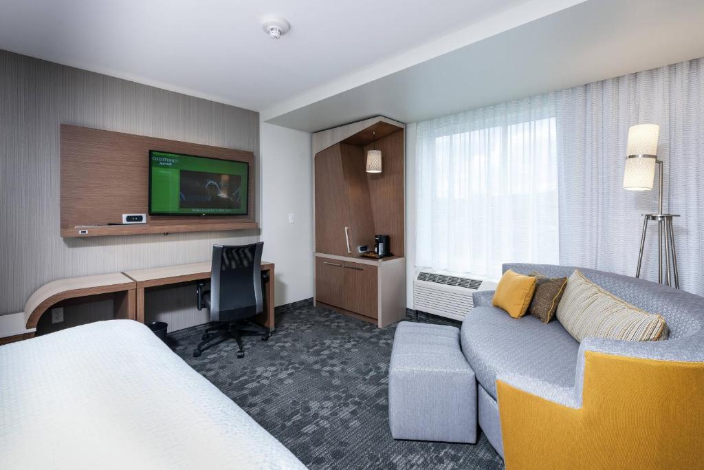a hotel room with a couch and a desk with a television at Courtyard by Marriott Boston Littleton in Littleton