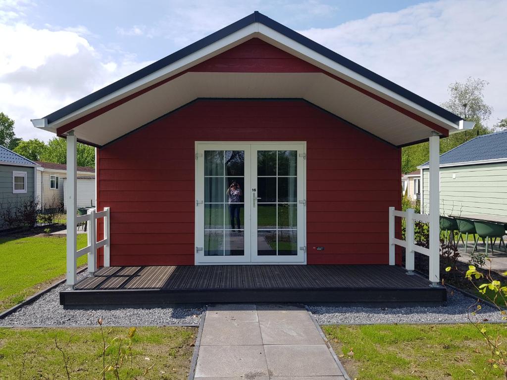 ein rotes Haus mit einer Veranda und einer Tür in der Unterkunft De Bijsselse Enk, Noors chalet 16 in Nunspeet