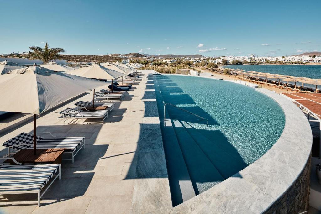 - une piscine avec des chaises longues et des parasols au bord de l'eau dans l'établissement Cosme, a Luxury Collection Resort, Paros, à Náoussa