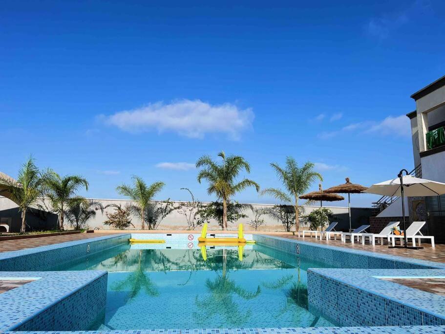 a swimming pool next to a beach with palm trees at Dar Sakina with Private Pool in Oulad Zenati