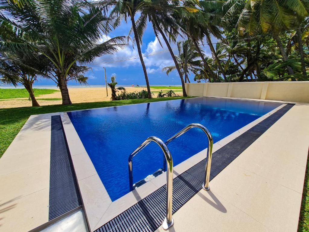 a swimming pool next to a beach with palm trees at Star Beach Guest House in Negombo