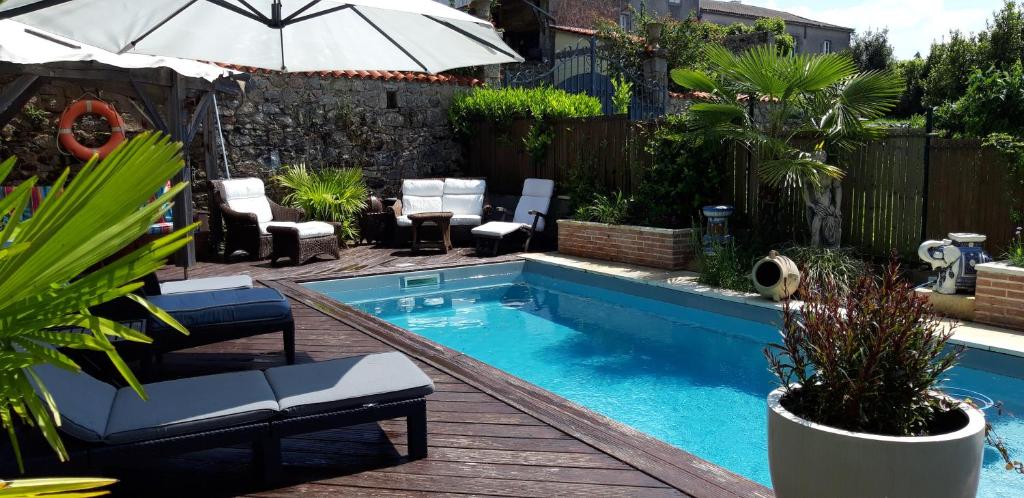 una piscina en un patio trasero con sillas y sombrilla en La Belle Maison en Piégut-Pluviers