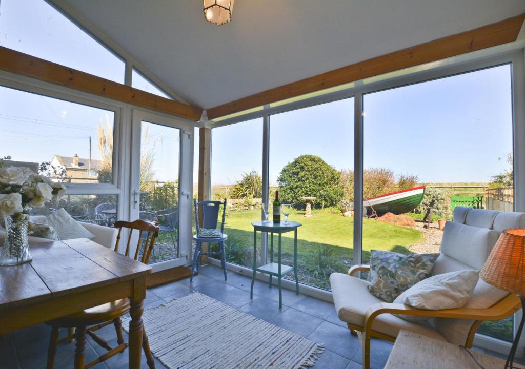 a living room with large windows and a table and chairs at Beach View Cottage in Amble