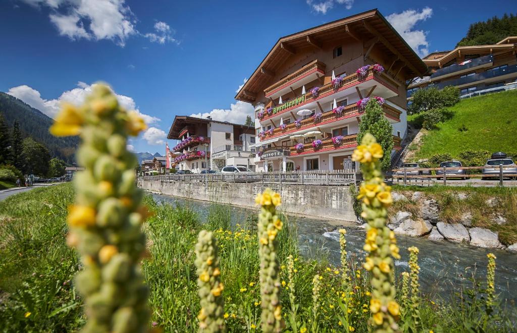 a building with flowers in front of a river at Apart-Hotel Forellenhof in Saalbach Hinterglemm