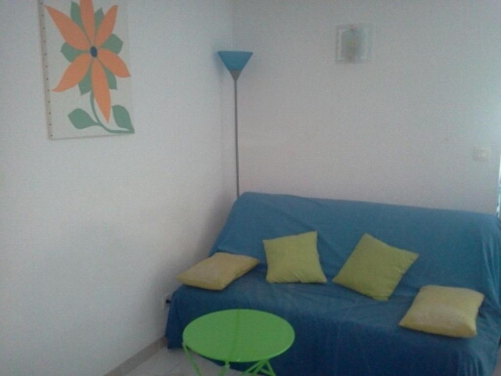 a room with a blue couch with yellow pillows and a table at Appartement F1 Calvi à 150 mètres de la plage in Calvi