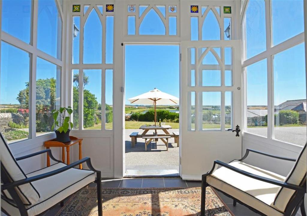 uma porta aberta para um pátio com 2 cadeiras e um guarda-sol em Carnevas Farmhouse em Saint Merryn