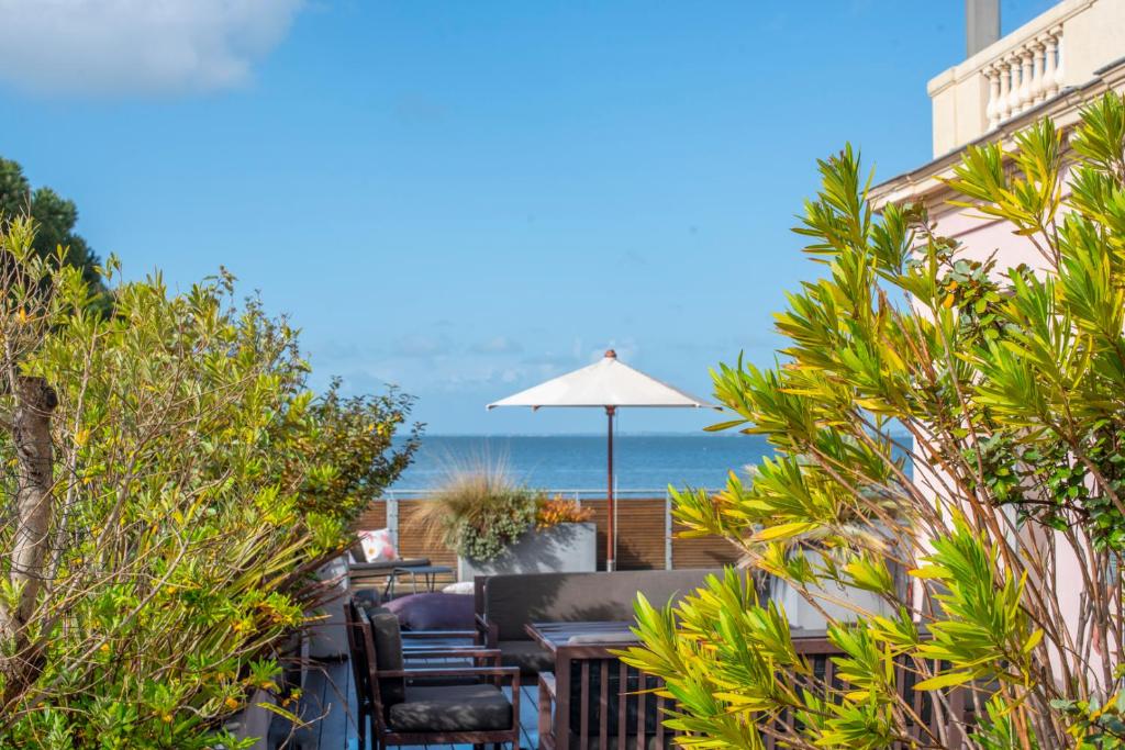 a patio with chairs and an umbrella and the ocean at Les Résidences première ligne in Andernos-les-Bains